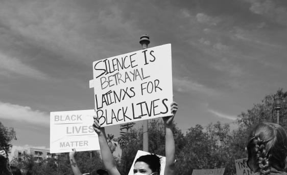 Person holding sign, "Silence is betrayal for Latinx and Black lives"