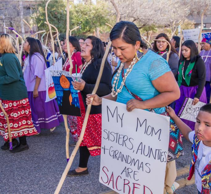 Woman holding sign, "My mom, sisters, aunties + grandmas are sacred'