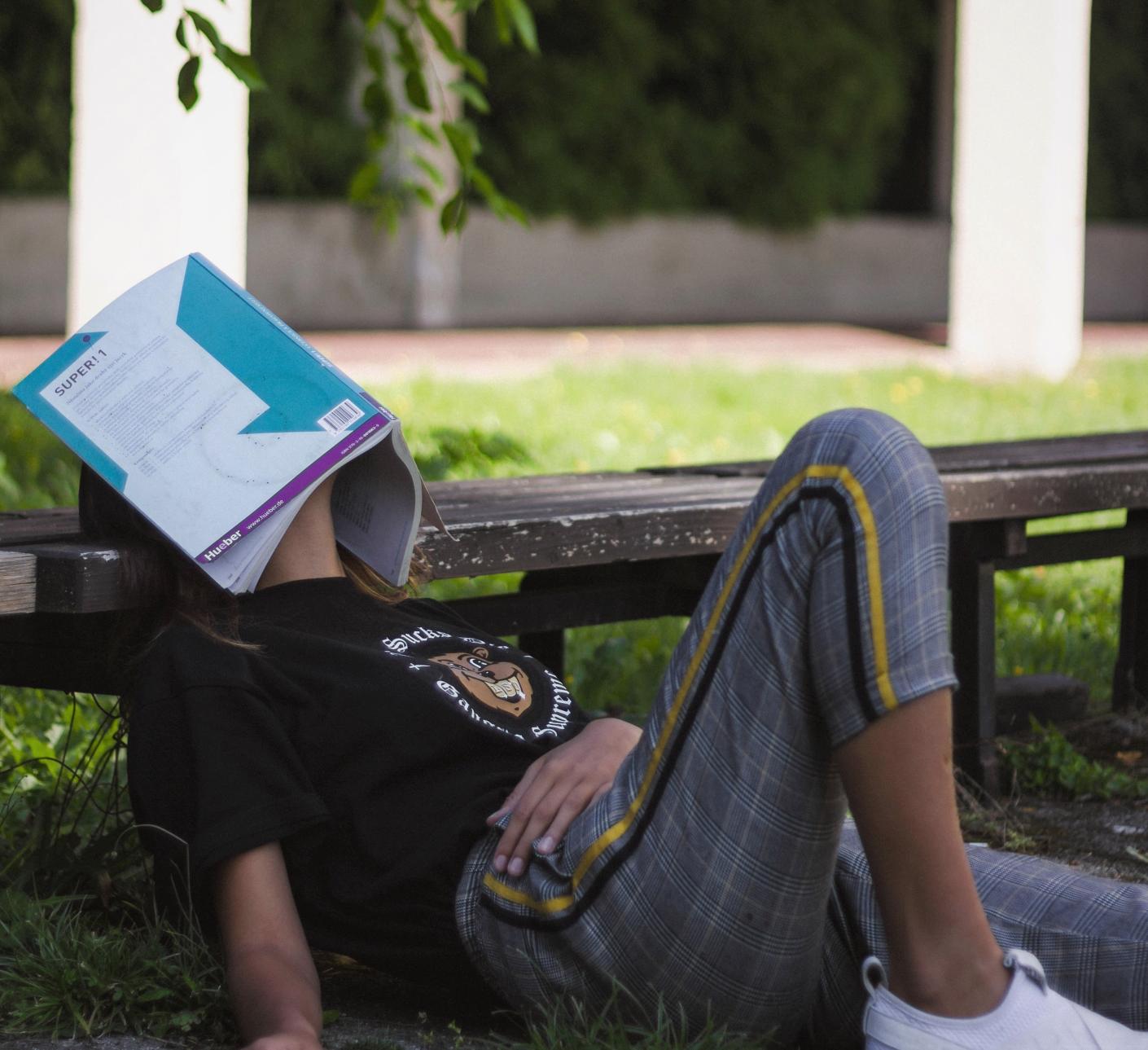 Student lays on the ground with a book over their face. 