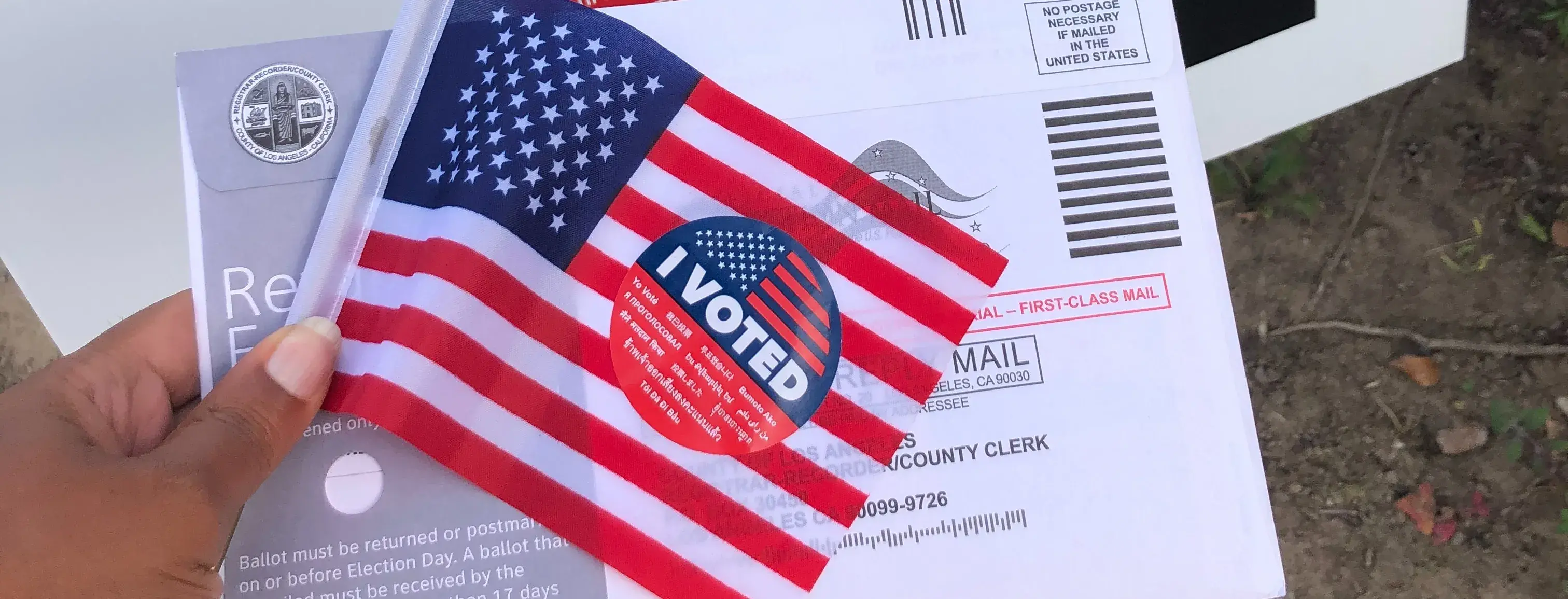 A person holds up an "I Voted" sticker, along with their ballot.